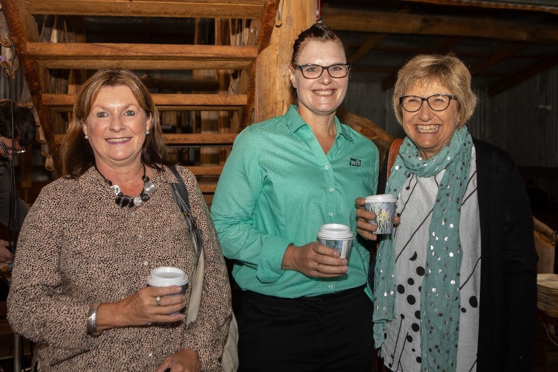 Three ladies standing by stairs with takeaway coffee