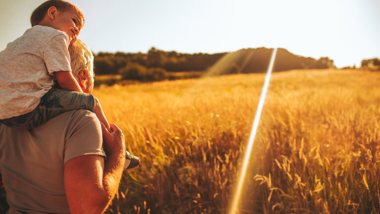 Kid on shoulder of grandfather in grain field