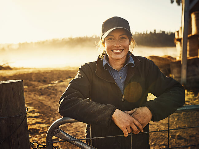 Young woman smiling at farmgate in morning sun